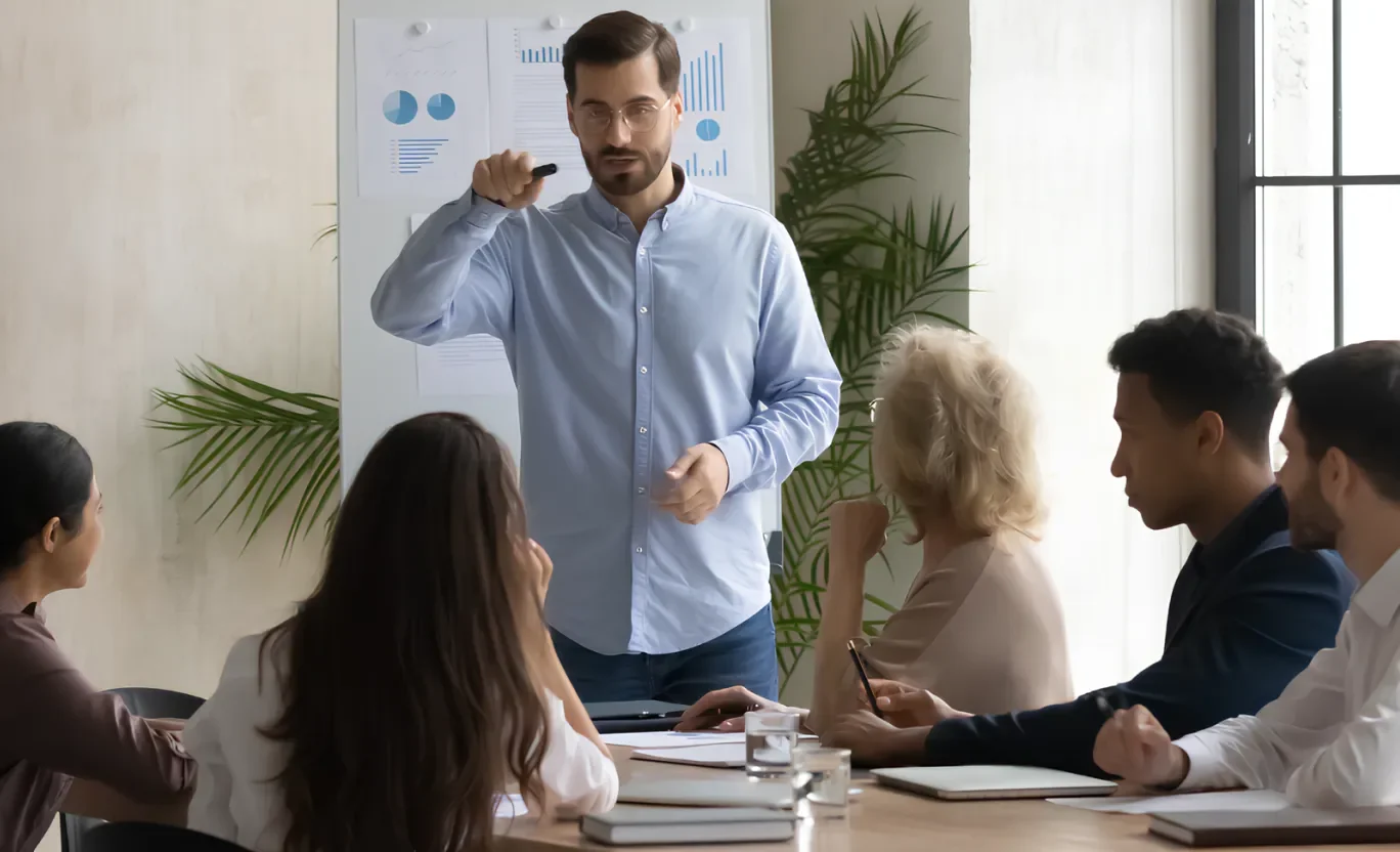 Meeting of 6 people with one presenting in front of a paper whiteboard 